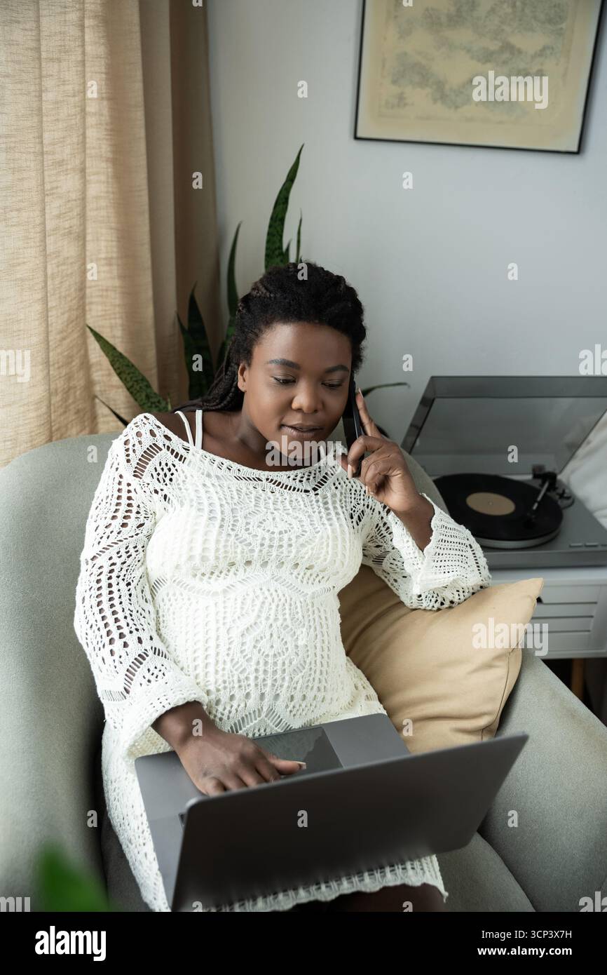 Une femme enceinte se détend à la maison, s'engageant avec son ordinateur portable pendant un appel. Banque D'Images