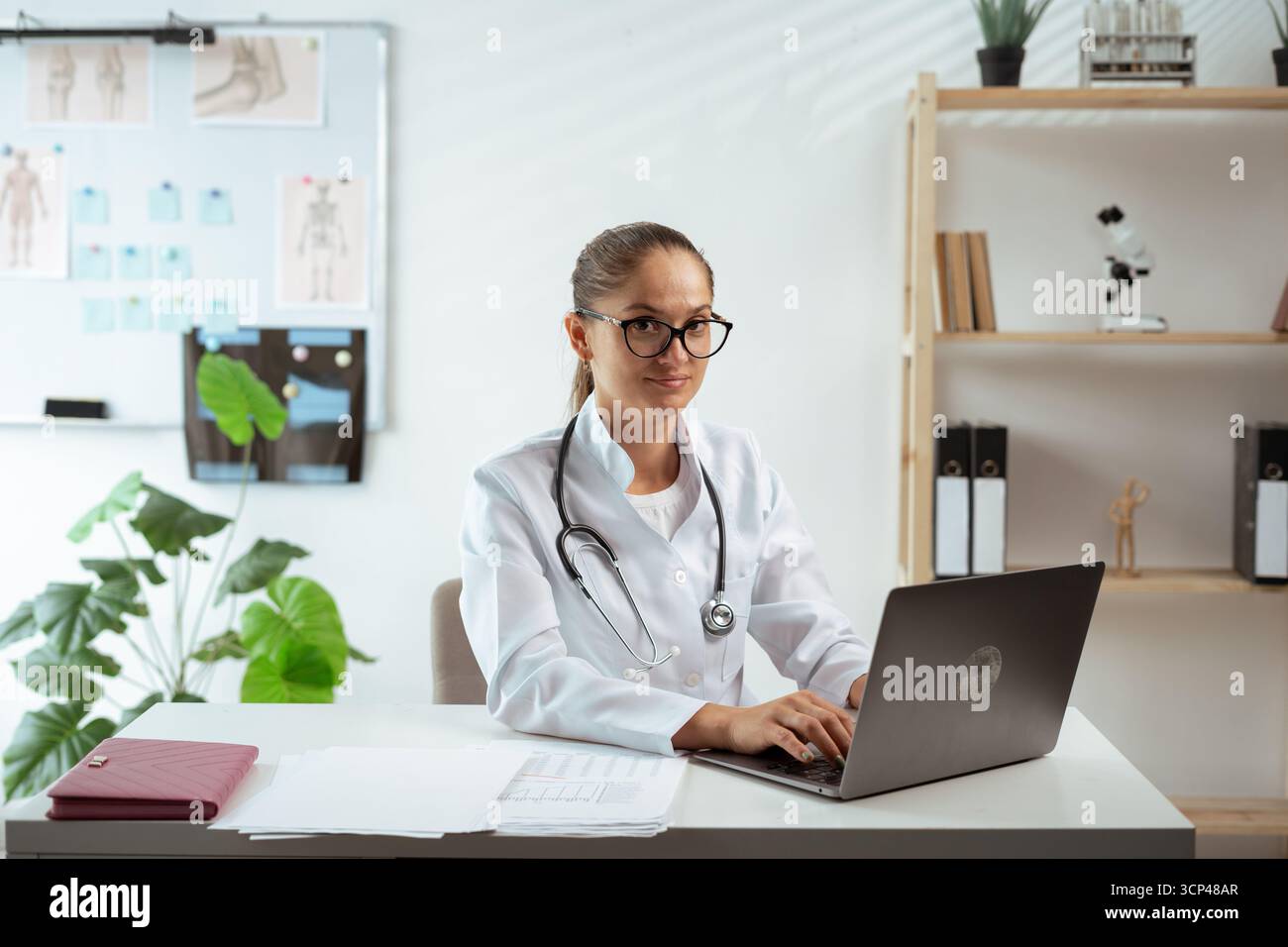Portrait d'un médecin féminin souriant avec ordinateur portable à table à l'hôpital. Consultation en ligne et concept de télémédecine Banque D'Images