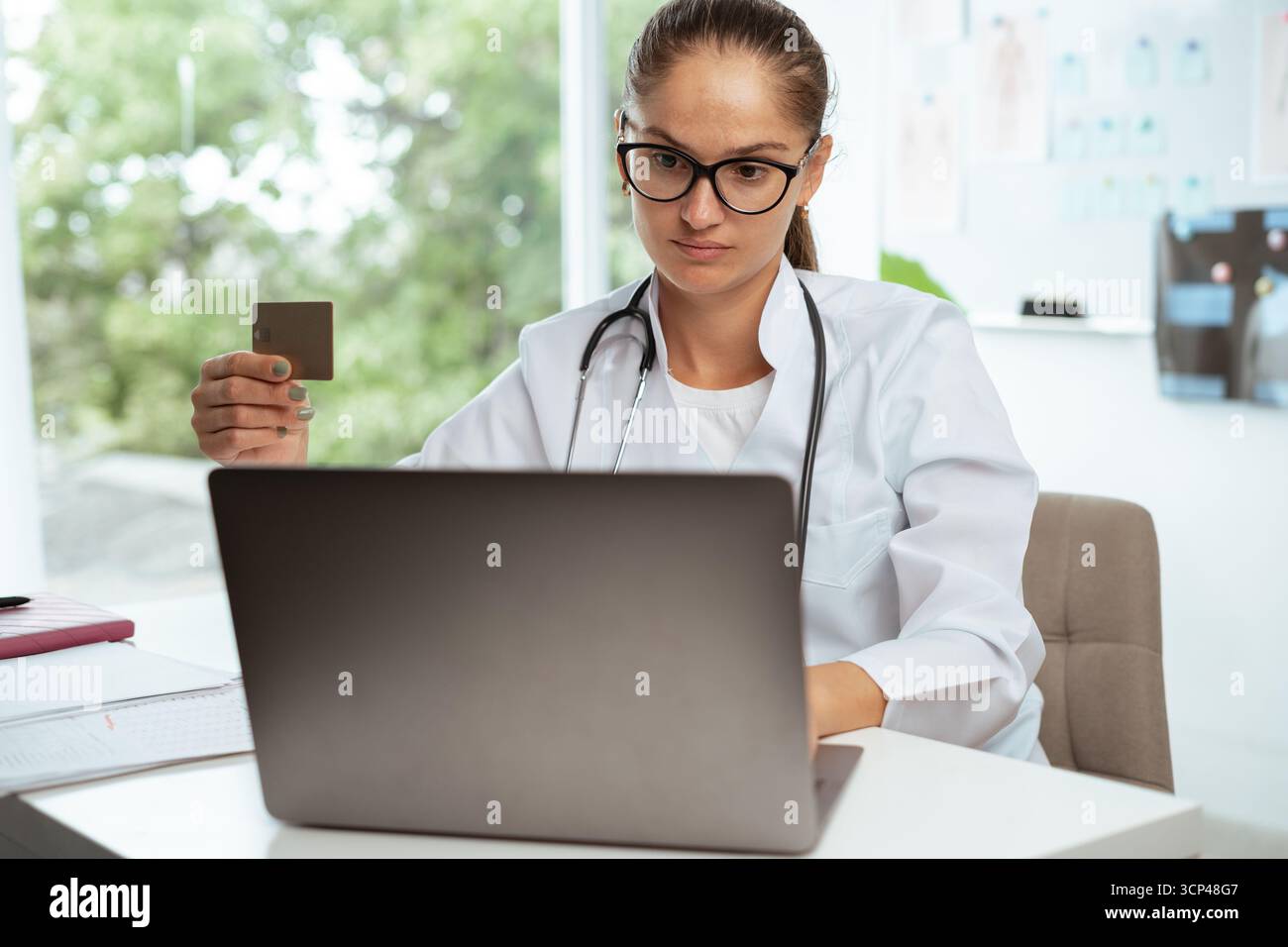 médecin ou infirmière en uniforme tenant une carte de crédit faisant des achats en ligne à l'aide d'un ordinateur portable dans son quart de travail. copier l'espace Banque D'Images