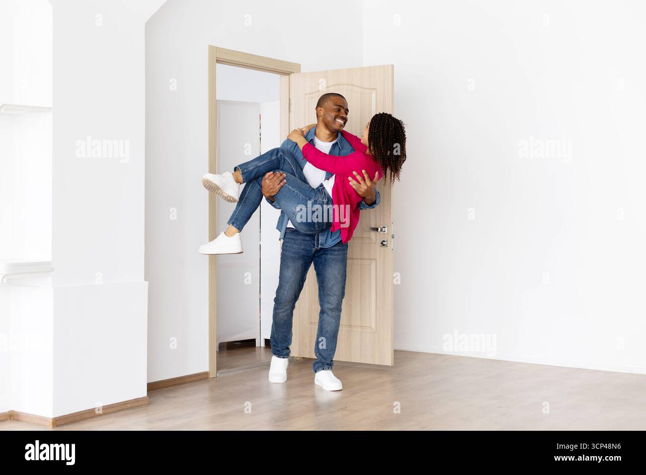 Homme noir heureux portant partenaire souriant dans les bras tout en entrant dans la nouvelle maison Banque D'Images