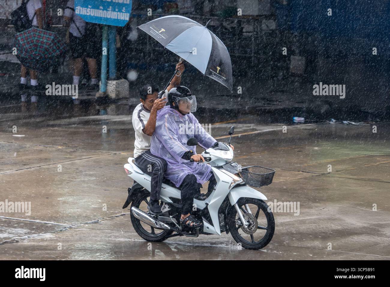 SAMUT PRAKAN, THAÏLANDE, JUIN 27 2025, deux personnes partageant un parapluie sur une moto sous la pluie Banque D'Images
