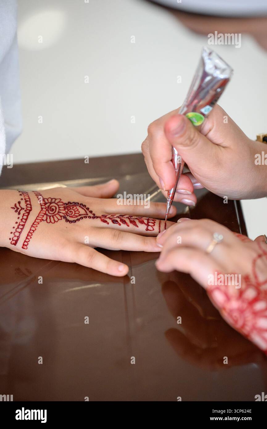 Le processus d'application de mehendi : l'artiste fait un tatouage temporaire au henné sur son bras. Gros plan : le maître dessine le henné sur la main d'une femme, traditionnel Banque D'Images