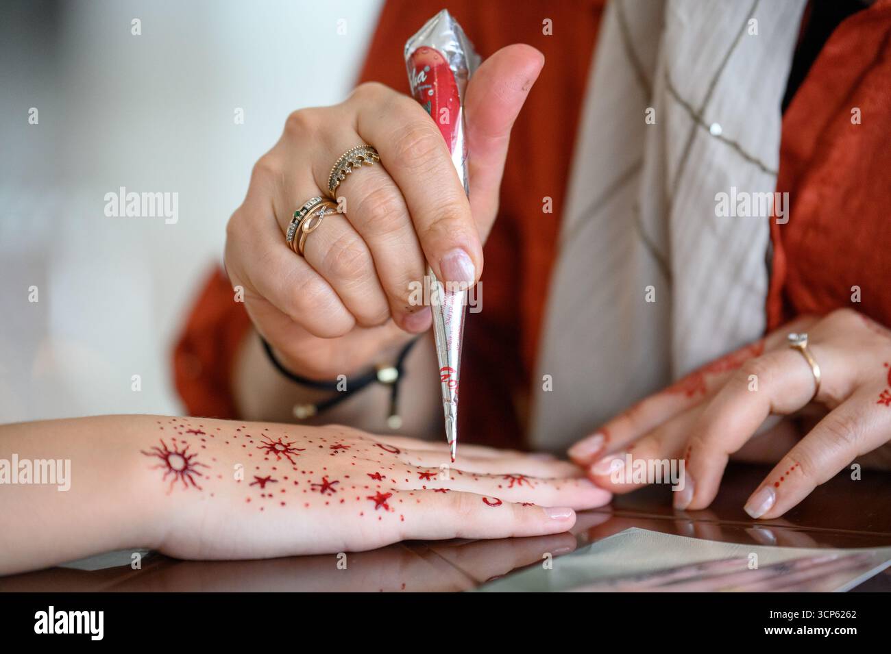 Le processus d'application de mehendi : l'artiste fait un tatouage temporaire au henné sur son bras. Gros plan : le maître dessine le henné sur la main d'une femme, traditionnel Banque D'Images
