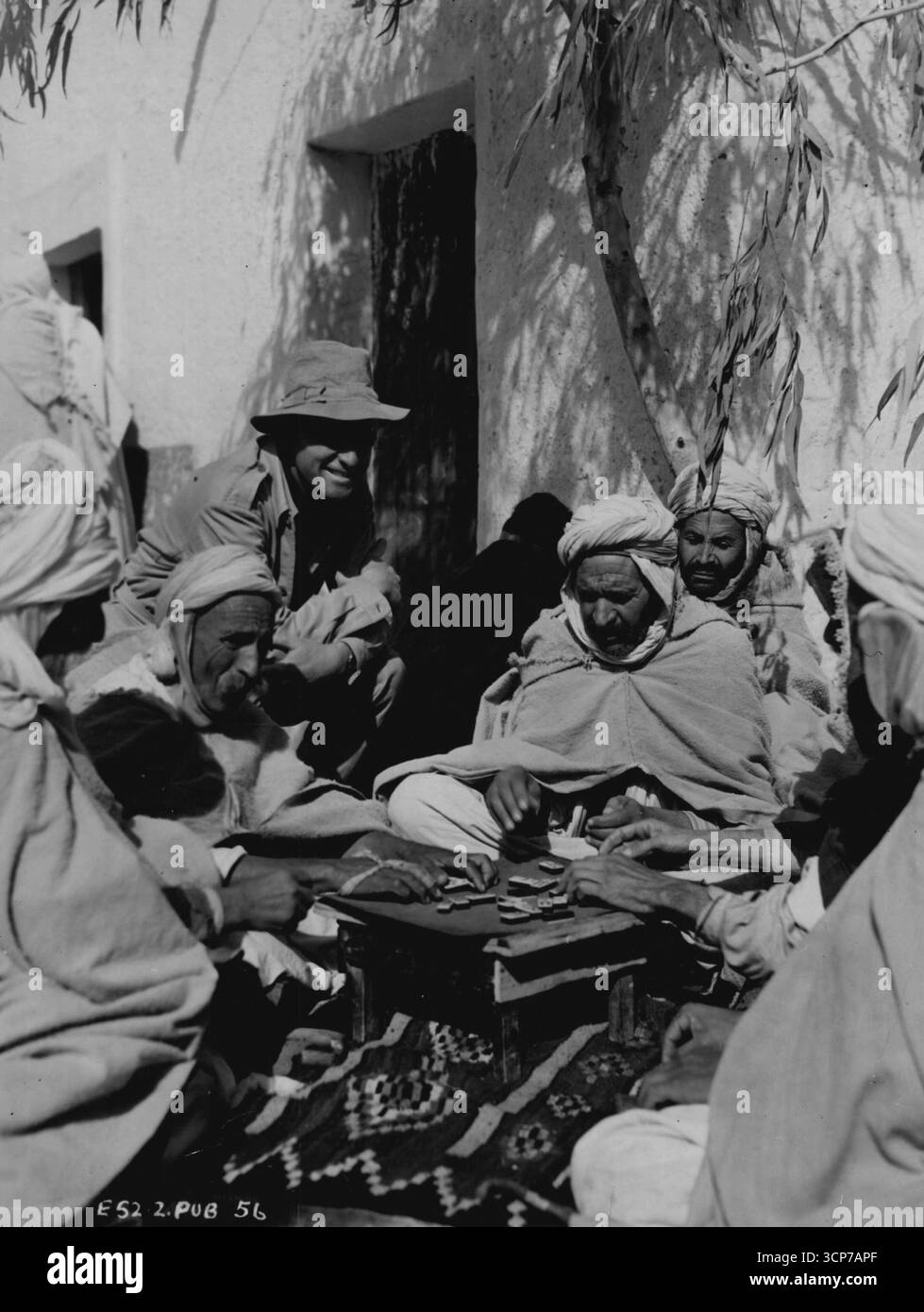 Star souriante d'Hollywood, Van Heflin, regarde un jeu de dominos joué par quatre Arabes âgés dans la ville de Bou Saada, en Afrique du Nord. Heflin était sur place pour le film 'Sud d'Alger', dans lequel il co-vedette avec Wanda Hendrix et Eric Portman. South of Alger est une production associée British-Mayflower réalisée par Jack Lee. 05 mai 1953. Banque D'Images