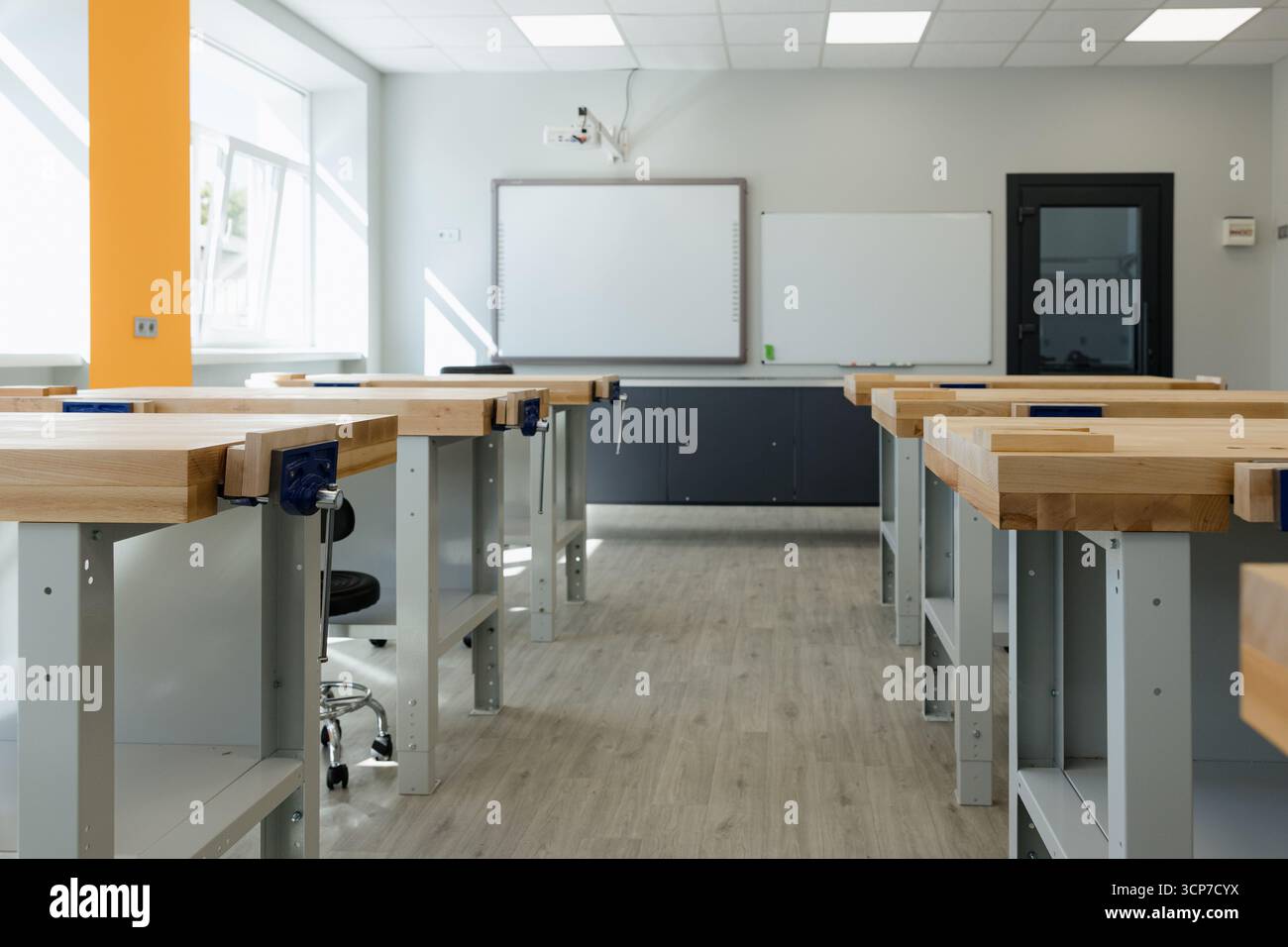 L'atelier lumineux dispose de grands bureaux en bois aménagés pour des projets créatifs, inondé de lumière naturelle provenant des fenêtres. Banque D'Images