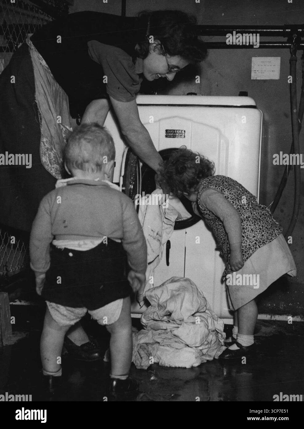 C'est là que vont les couches -- MRS Eleanor Miller, une locataire de Naylor House, Southwark, Londres, montre David, 1, et Pamela, 2 ans, comment elle utilise une des nouvelles machines à laver IS-in-the-slot. Naylor House est le premier des blocs d'appartements municipaux de Londres à être équipé de ces machines - il en a trois, à partager par vingt-quatre familles. En quarante-cinq minutes, la machine savonne, lave, effectue trois rinçages et sèche à l'humidité 9 livres de linge. D'autres appartements à Hammersmith et Bletchley, Bucks, les installent également, et ils sont envisagés pour Bermondsey ad Lambeth. 12 mars 1948. (Photo Banque D'Images