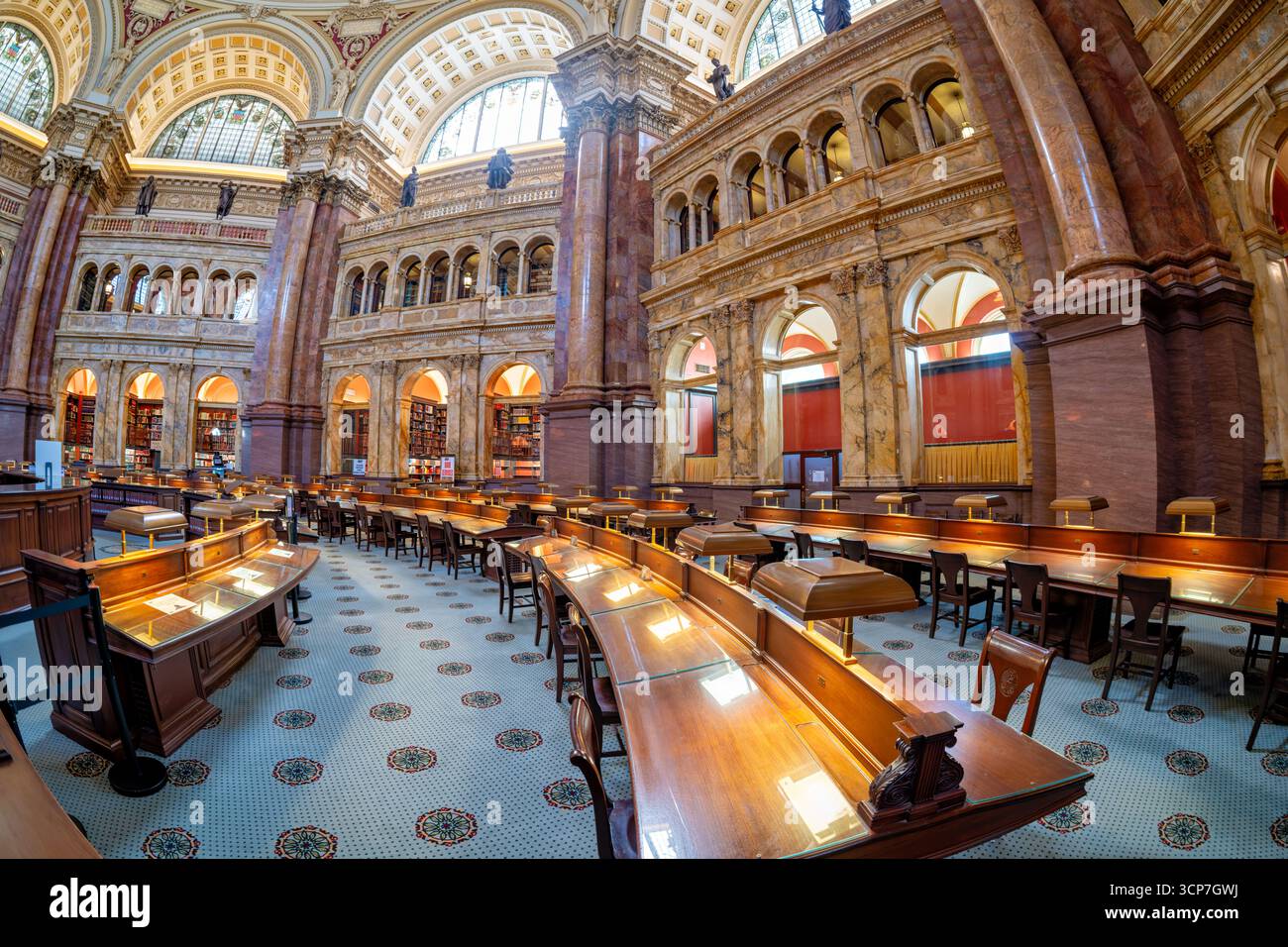 Bibliothèque du Congrès salle de lecture principale Fisheye Washington DC // WASHINGTON DC — la salle de lecture principale de la Bibliothèque du Congrès offre une vue fisheye de son intérieur grandiose, avec des rangées de bureaux en bois équipés de lampes traditionnelles. L'architecture comprend des colonnes de marbre ornées, des fenêtres cintrées avec des vitraux et des balcons donnant sur le vaste espace. Des étagères remplies de nombreux volumes bordent les murs, accessibles depuis les niveaux supérieurs. Le plafond complexe et la moquette à motifs contribuent à son atmosphère majestueuse. La Bibliothèque du Congrès, créée en 1800, est Banque D'Images