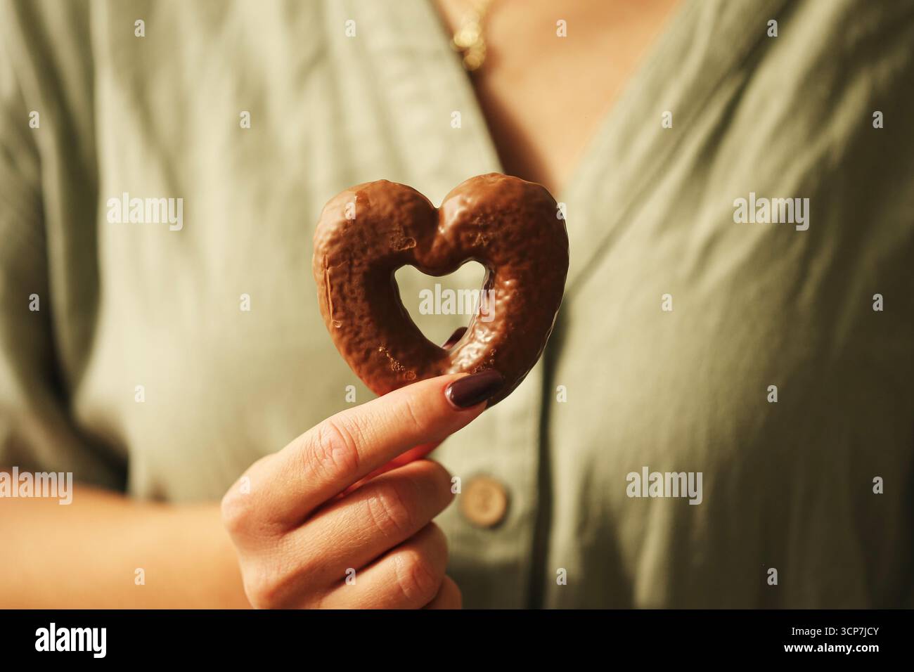 Femme tenant un biscuit en forme de coeur. Mains féminines avec pain d'épice cuit symbole de l'amour. Dessert sucré en gros plan. Concept romantique de l'affection. Banque D'Images