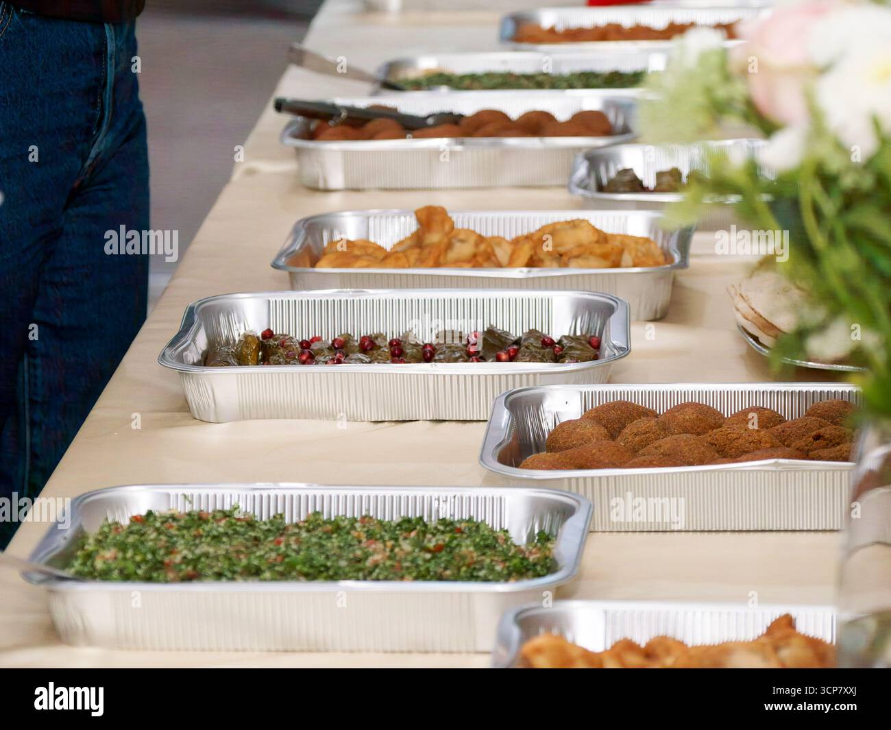 Buffet mezzé libanais avec taboulé, falafel, feuilles de vigne, samosas et pain pita dans des plateaux en aluminium lors d'un événement traiteur. Banque D'Images