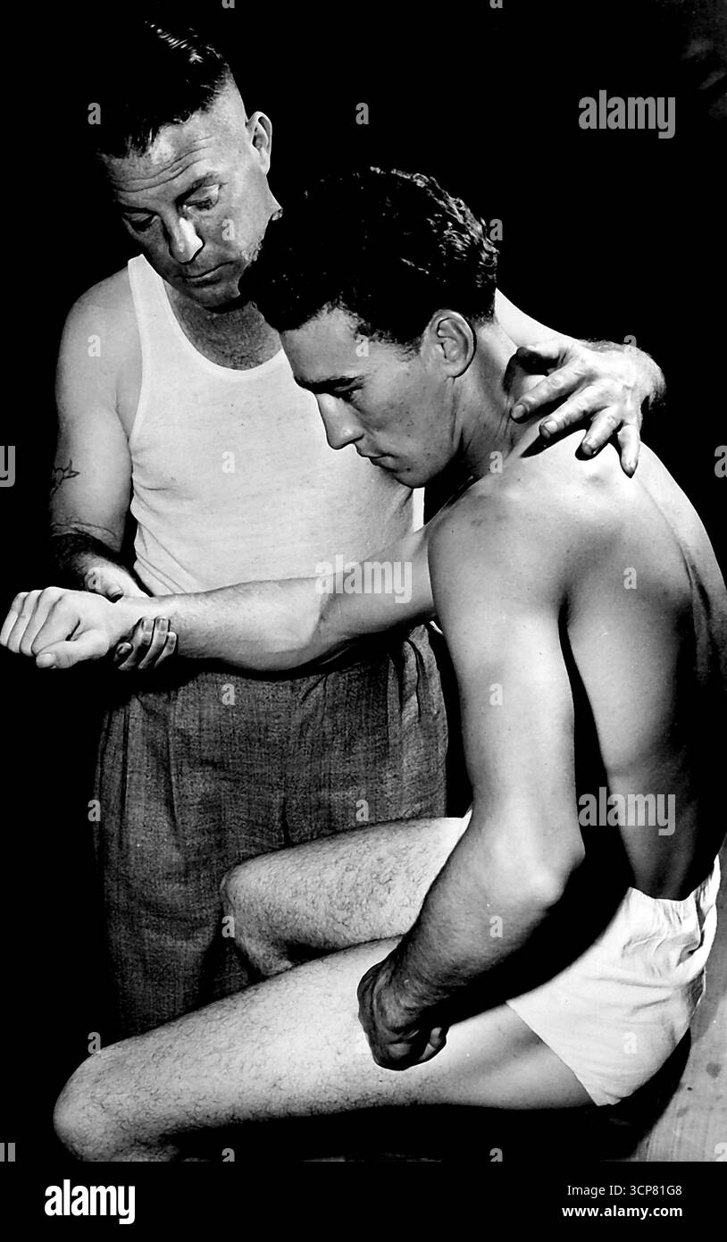 Le champion des poids légers Colin Clarke a reçu une pesée à midi pour le combat de stade de lundi soir avec Don McTaggart. Clarke a déclaré à la direction du stade que, comme il vivait à Kenthurst, près de Windsor, il serait tard chez lui pour le déjeuner si la pesée était tenue à l'heure normale, 14 heures. Colin aime apparemment cuisiner à la maison quand il doit faire tant de voyages en une journée. La photo montre l'entraîneur Billy Lawrence massant Clarke pendant une séance de gymnase. 1er février 1955. Banque D'Images