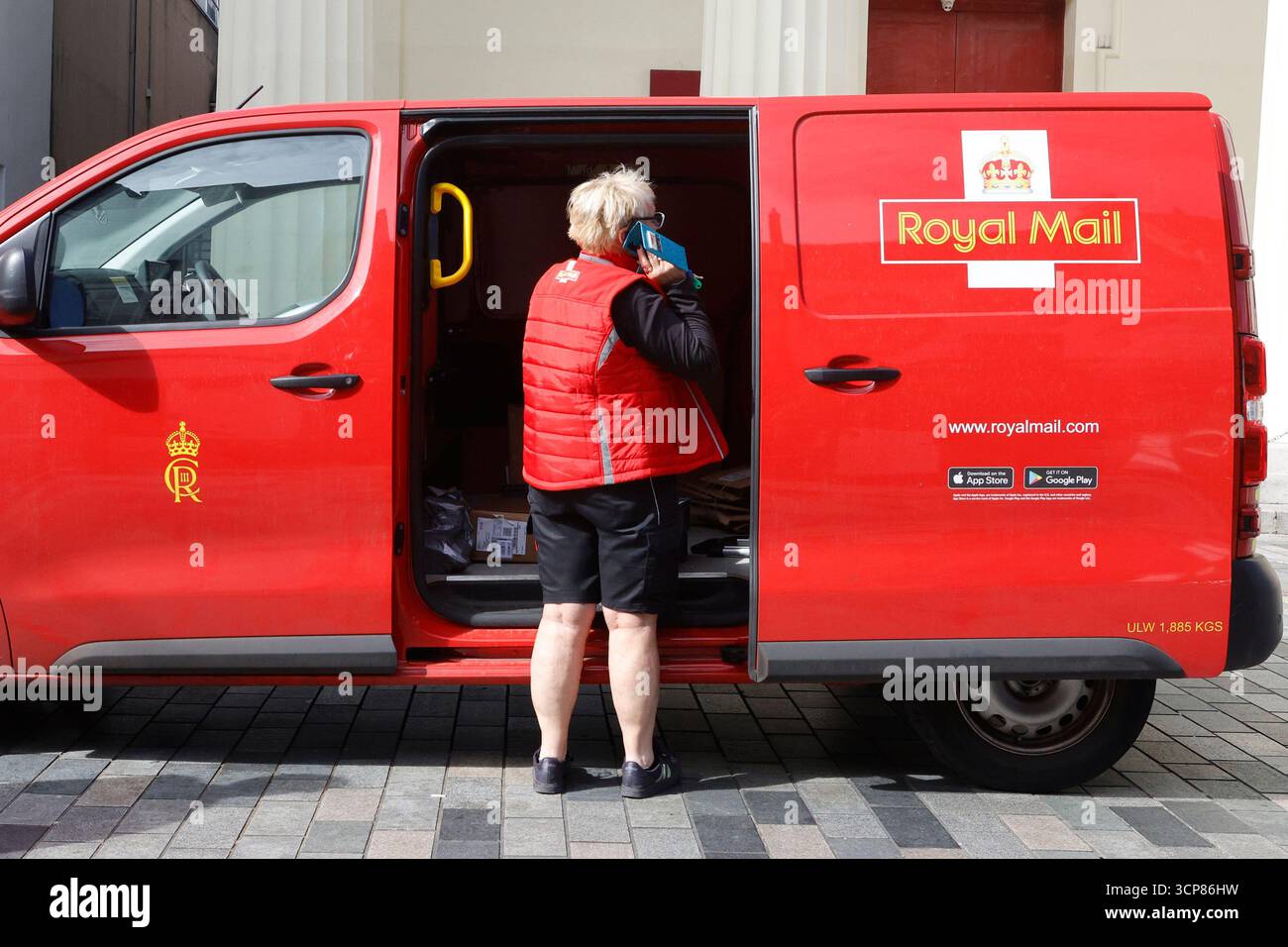 Travailleur des postes sur un téléphone portable à côté de son fourgon de livraison Banque D'Images