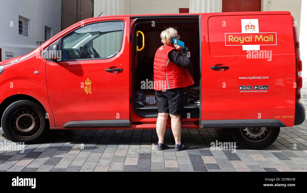 Travailleur des postes sur un téléphone portable à côté de son fourgon de livraison Banque D'Images