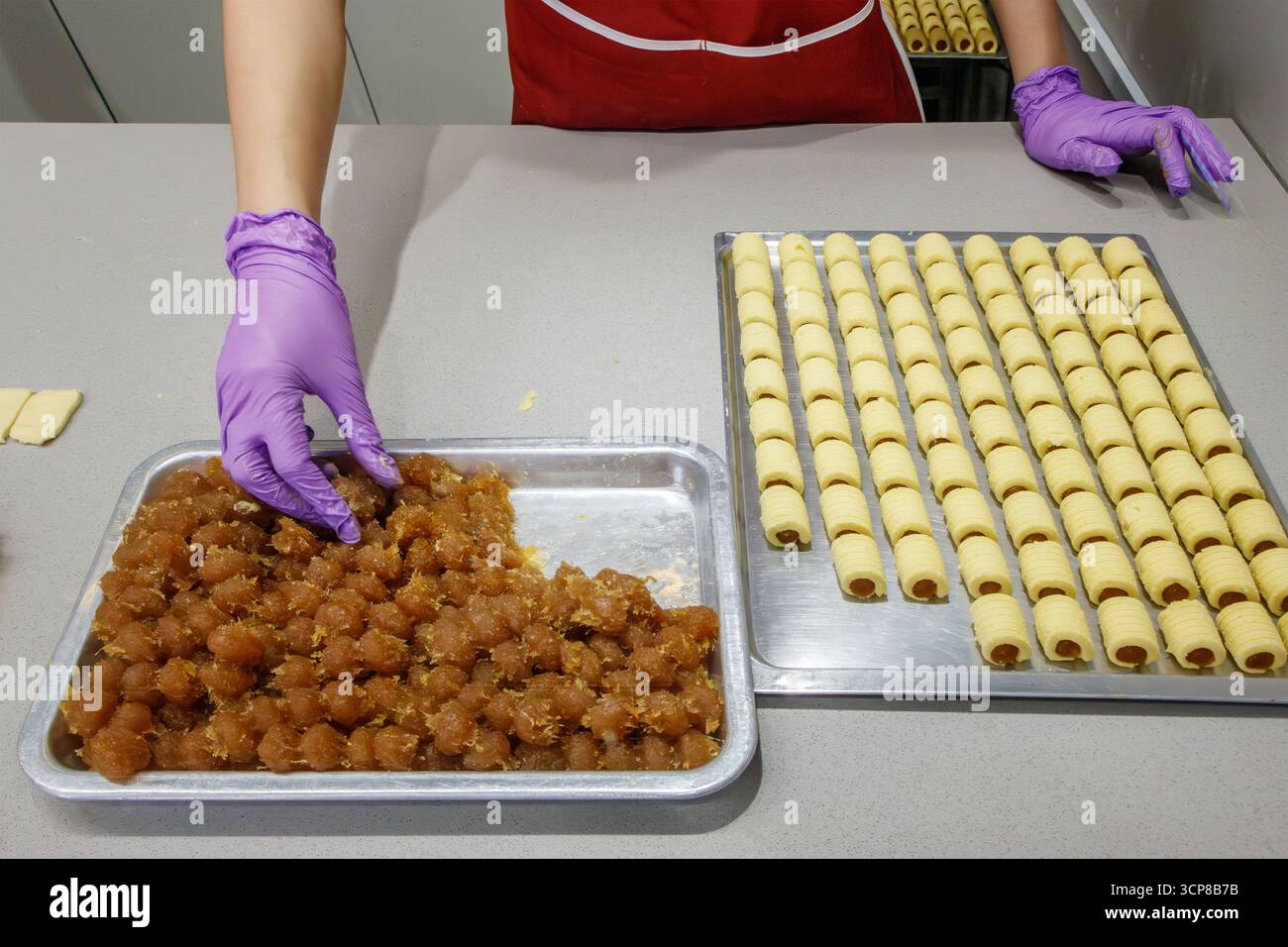 Personne portant des gants violets préparant des pâtisseries roulées avec un plateau de remplissage d'ananas dans une cuisine ouverte cuisine de rue malacca malaysia Banque D'Images