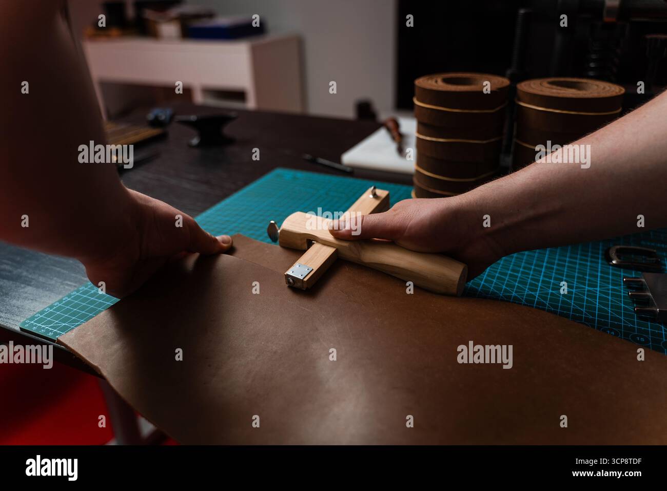 Préparation de ceinture en cuir à la main avec coupe-sangle en bois sur le tapis de coupe. Artisan coupe la bande de cuir avec un outil en bois. Artisan préparant leat Banque D'Images