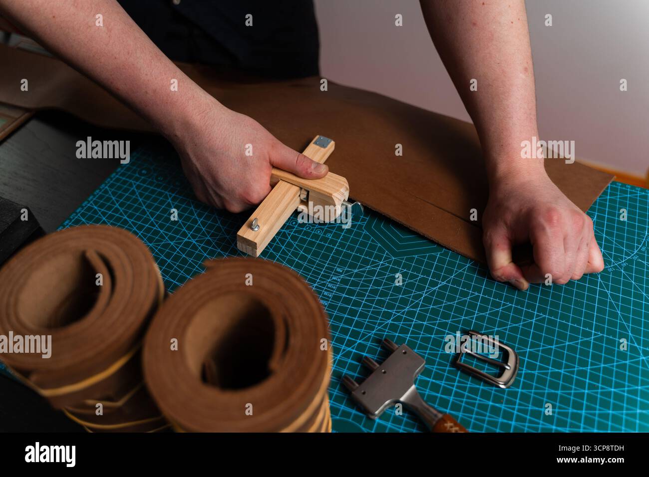 Préparation de ceinture en cuir à la main avec coupe-sangle en bois sur le tapis de coupe. Artisan coupe la bande de cuir avec un outil en bois. Artisan préparant leat Banque D'Images