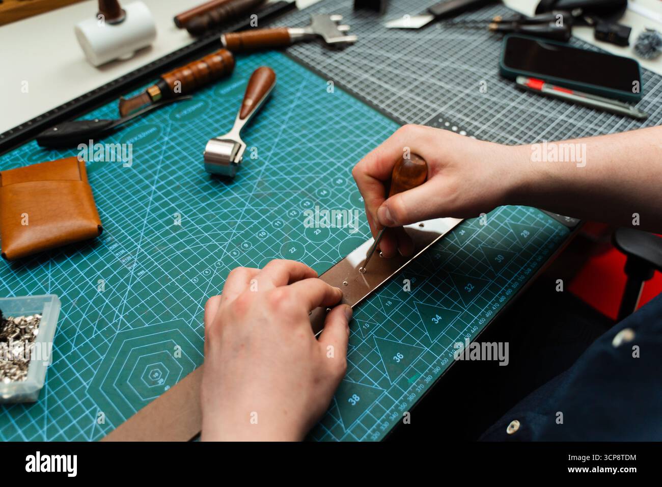 Poinçonnage et détail des trous de ceinture en cuir. Artisan poinçonnant des trous dans un bracelet en cuir pour une ceinture faite à la main sur un tapis de coupe vert. Fraisage des trous du tapis Banque D'Images
