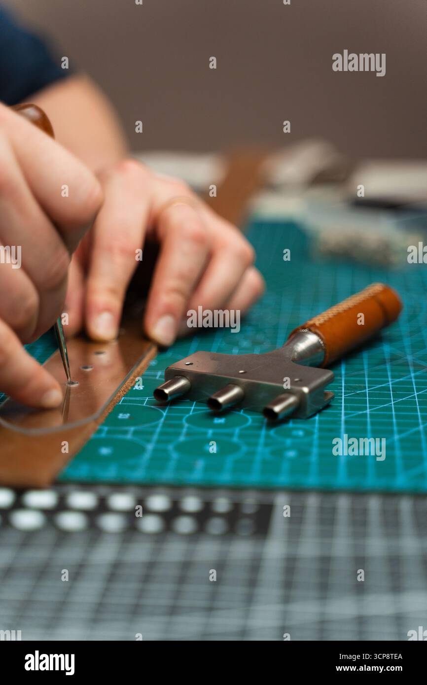 Poinçonnage et détail des trous de ceinture en cuir. Artisan poinçonnant des trous dans un bracelet en cuir pour une ceinture faite à la main sur un tapis de coupe vert. Fraisage des trous du tapis Banque D'Images