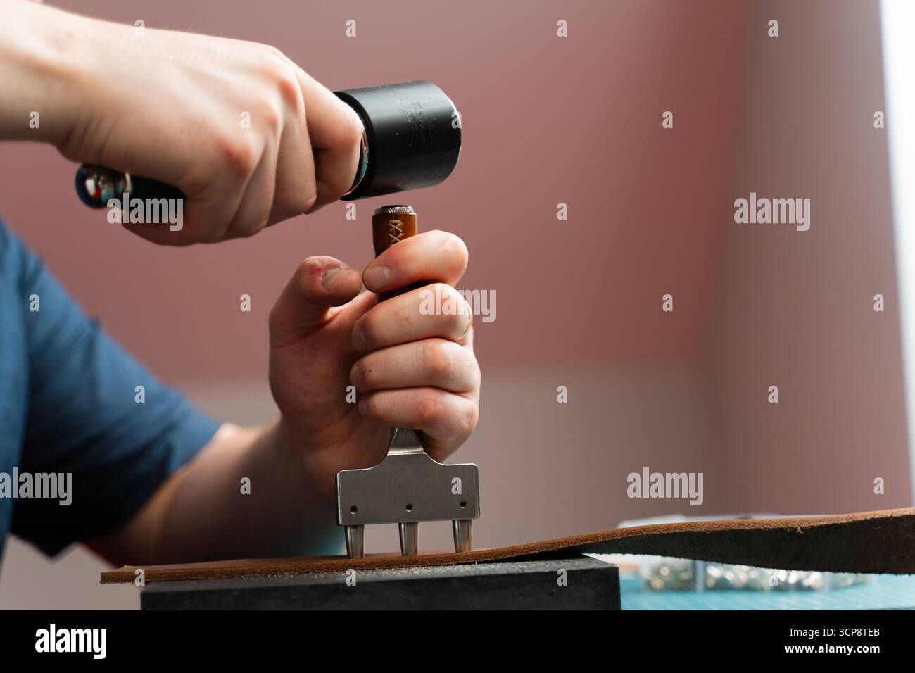 Poinçonnage et détail des trous de ceinture en cuir. Artisan poinçonnant des trous dans un bracelet en cuir pour une ceinture faite à la main sur un tapis de coupe vert. Fraisage des trous du tapis Banque D'Images