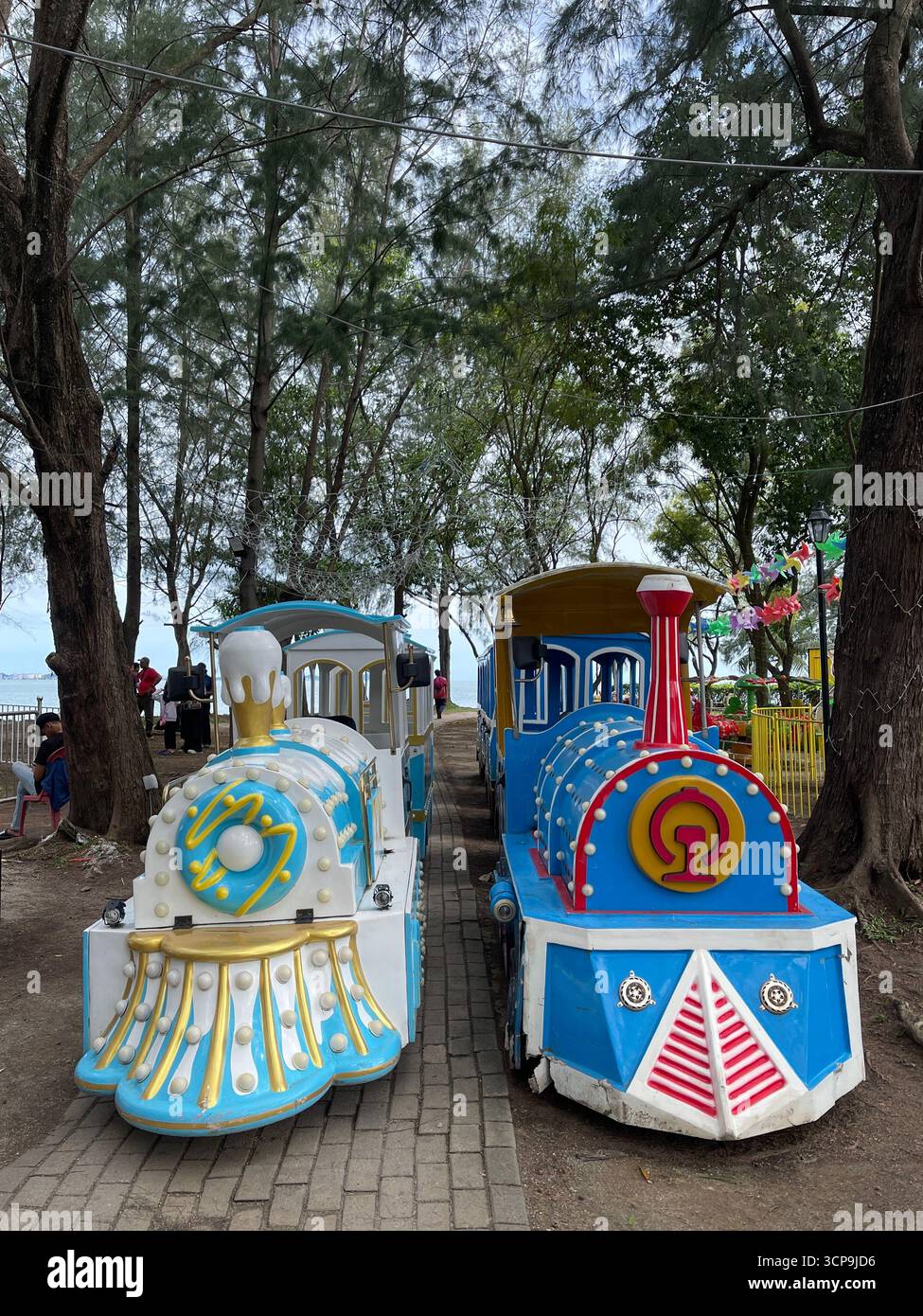 Port Dickson, Malaisie - 15 septembre 2025 : trains pour enfants colorés alignés sous les arbres au PD Waterfront Carnival. - Image de stock capturée avec un smartphone