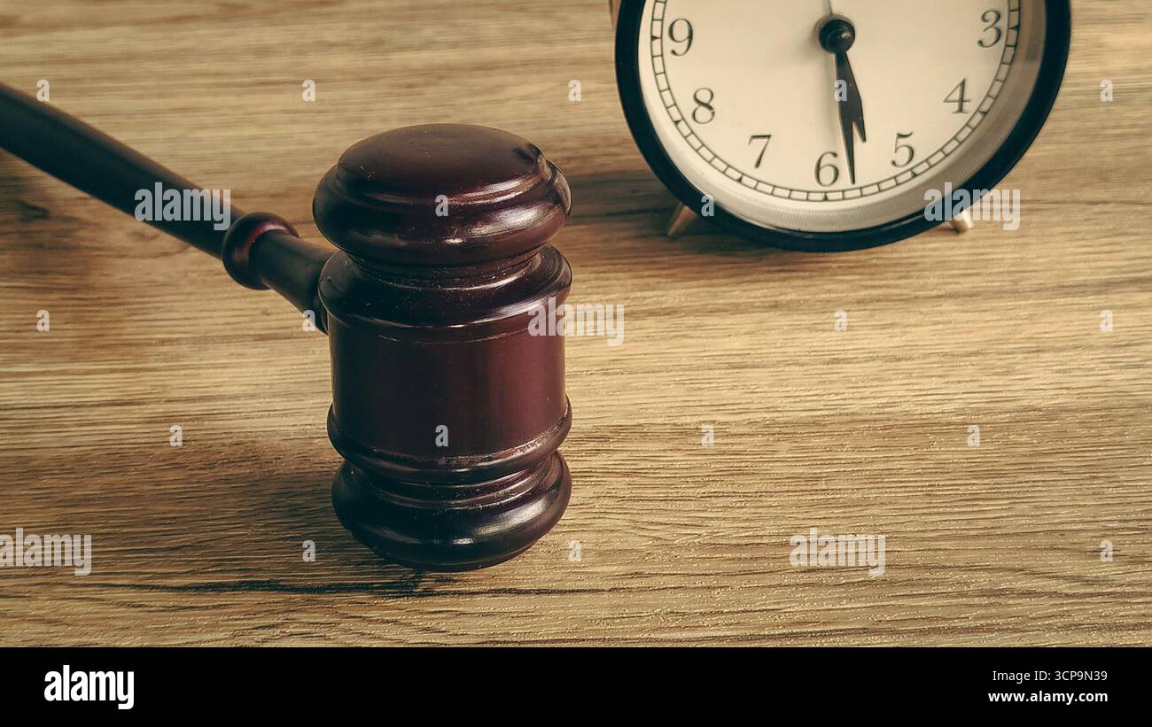 Marteau et réveil sur une table en bois, symbolisant un délai légal ou une affaire judiciaire urgente. Banque D'Images