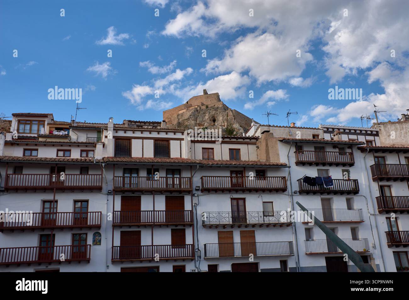 La vibrante place Pla de Estudi à Morella prend vie sous un ciel bleu parsemé de nuages blancs, mettant en valeur un groupe de bâtiments traditionnels Banque D'Images