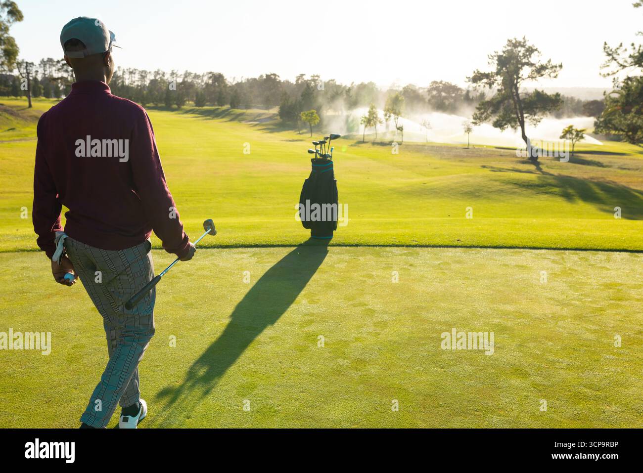 Homme afro-américain debout sur putting green près du sac de golf tenant putter, espace de copie Banque D'Images
