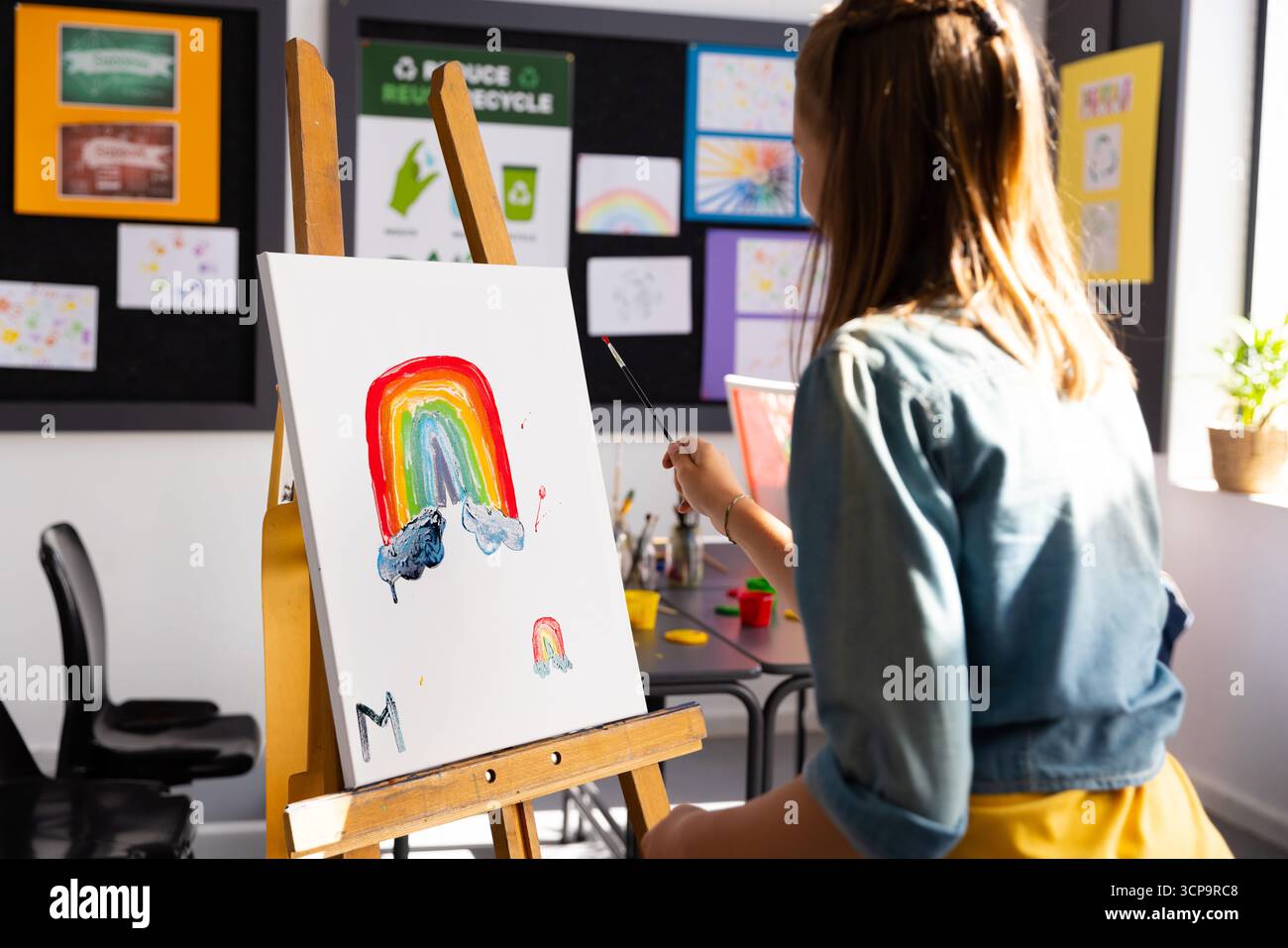 Fille d'âge scolaire peignant arc-en-ciel sur toile au chevalet en bois dans la classe d'art avec pinceau, espace de copie Banque D'Images