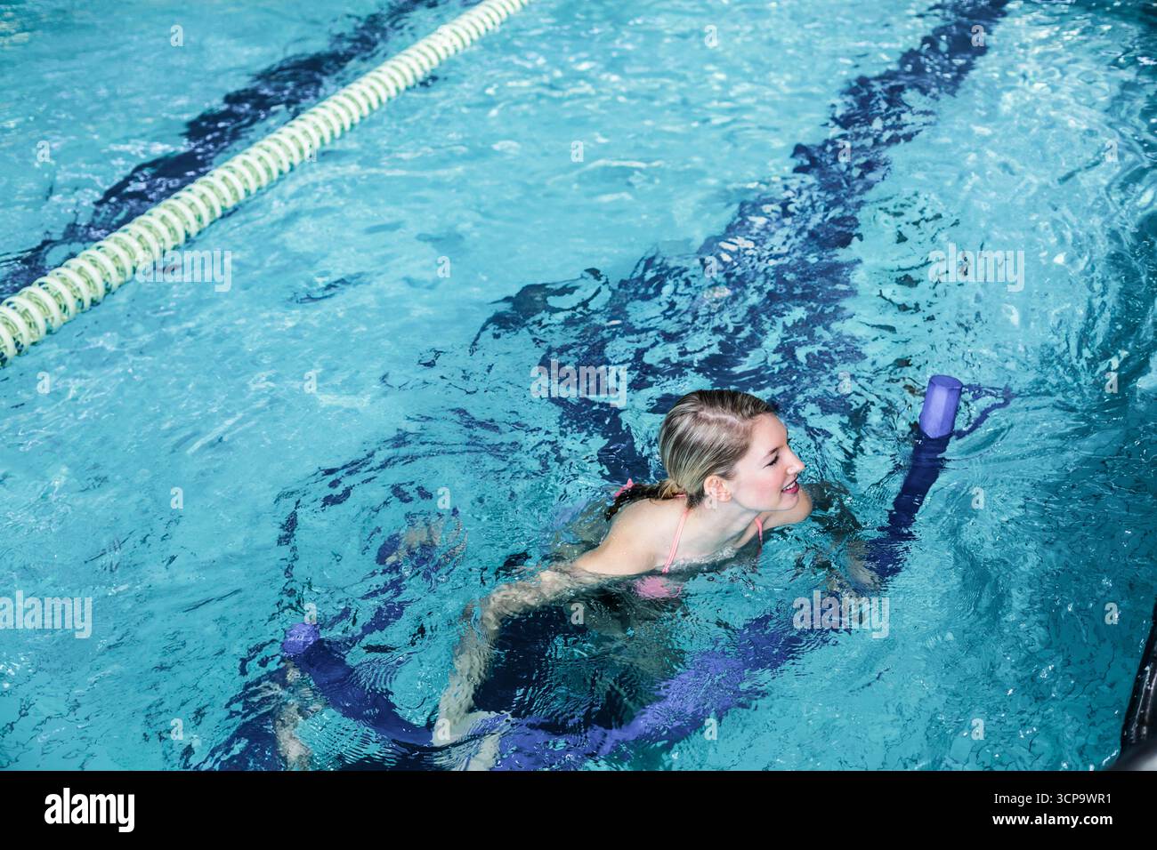 Nouilles de piscine en mousse violette flottant dans une voie bleue, avec des ondulations se formant près du diviseur vert et blanc Banque D'Images