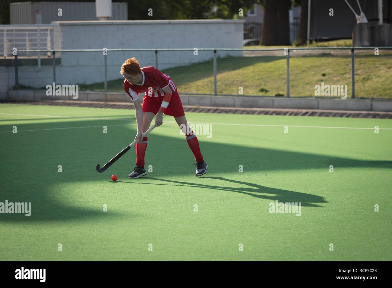 Joueur masculin de hockey sur gazon se penchant vers l'avant, agrippant le bâton, se concentrant sur la balle rouge sur le gazon Banque D'Images