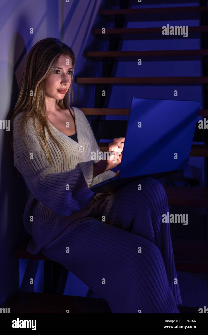 Jeune femme dans les escaliers tape le pavé tactile dans la lumière bleue. Mise au point nuit. Banque D'Images