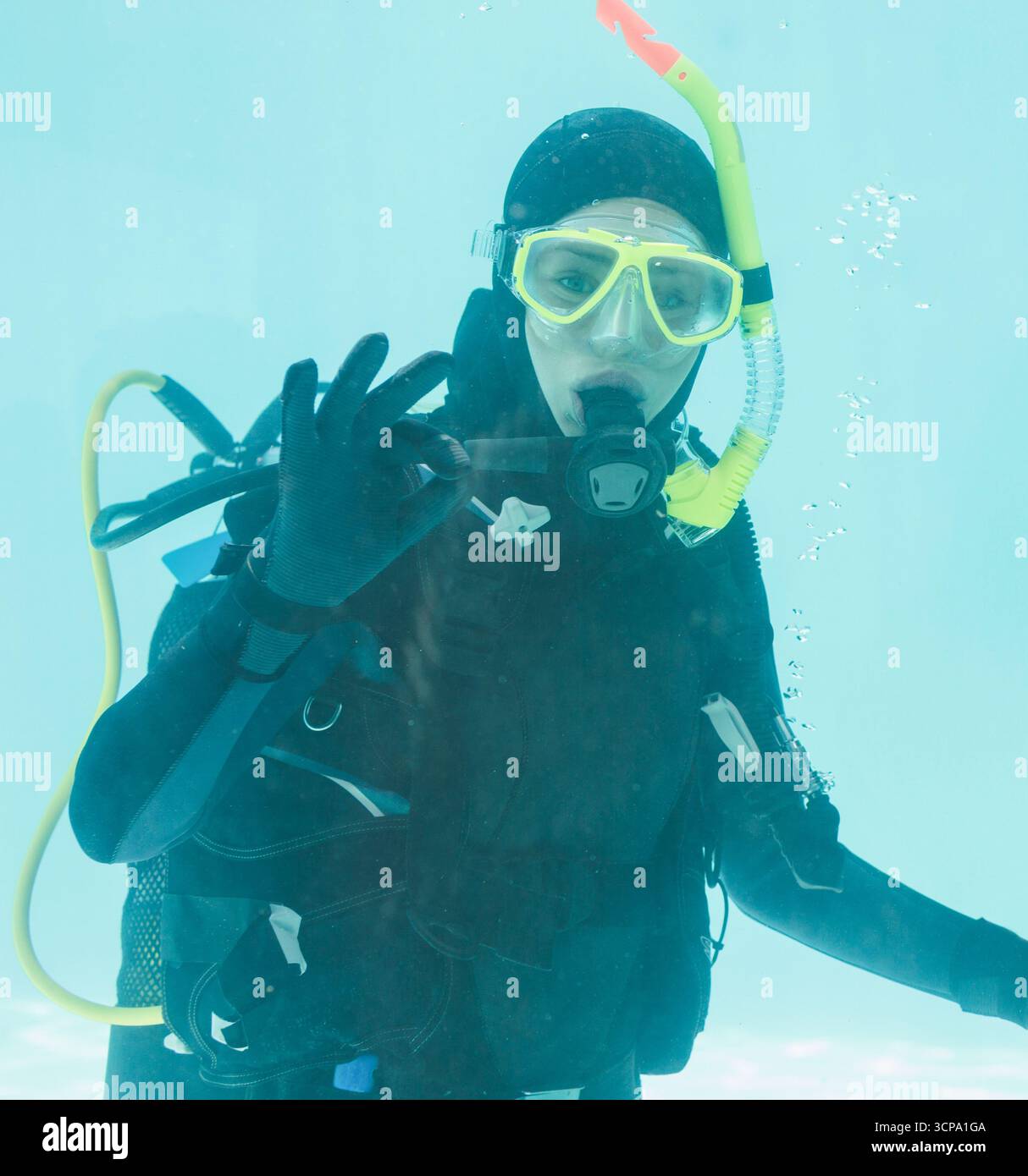 Plongée sous-marine signale OK sous l'eau avec masque de plongée jaune et régulateur dans la piscine turquoise Banque D'Images