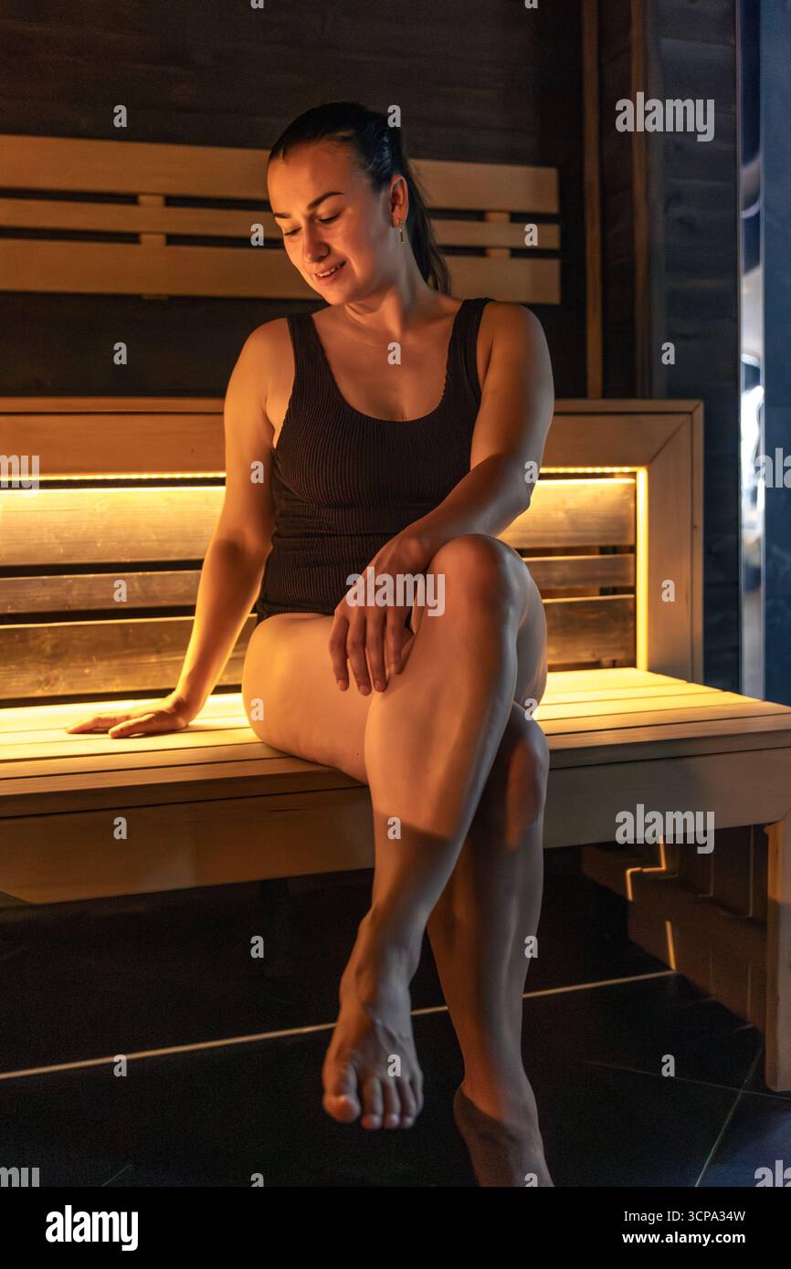 Femme dans le sauna avec un sourire doux, lueur ambre. Calme chaud. Banque D'Images