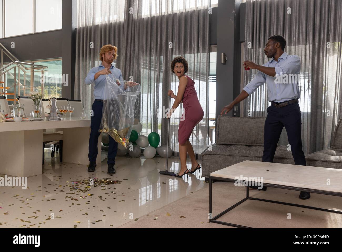 Divers amis nettoyant des confettis métalliques dans le salon moderne avec balai, sac poubelle Banque D'Images