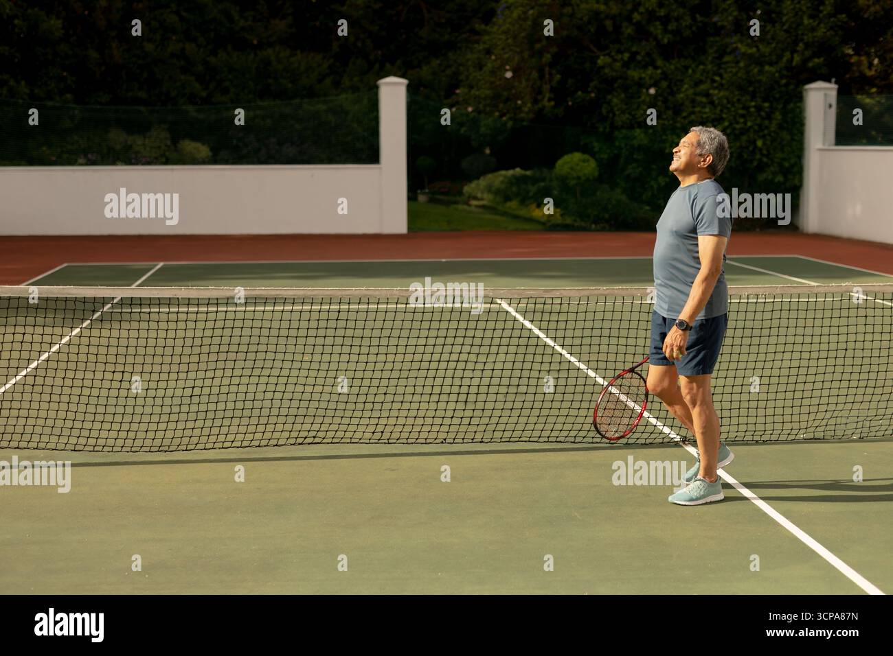 Homme senior debout sur un court de tennis tenant une montre de sport de raquette regardant vers le haut, espace de copie Banque D'Images