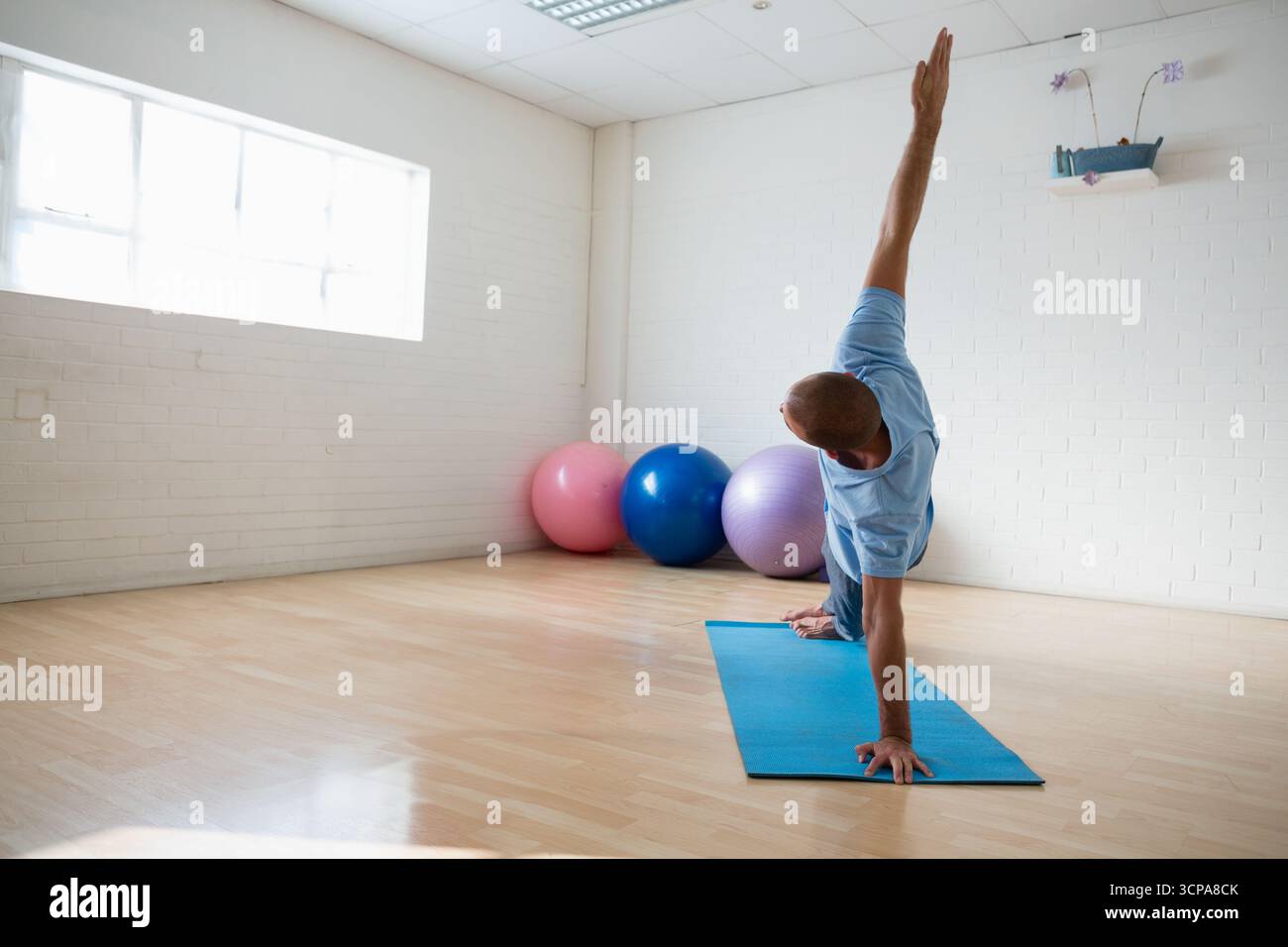 Homme effectuant une planche latérale sur tapis bleu dans un studio de yoga avec des boules pastel, plante, espace copie Banque D'Images