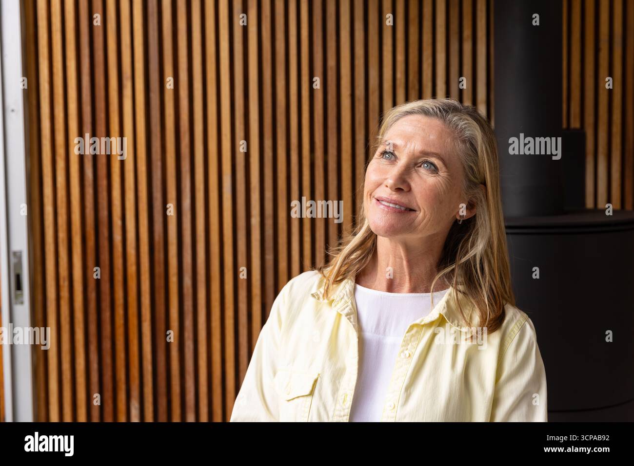 Femme senior regardant vers le haut contre le mur de lattes à l'intérieur avec tuyau de poêle sur la droite, copiez l'espace Banque D'Images