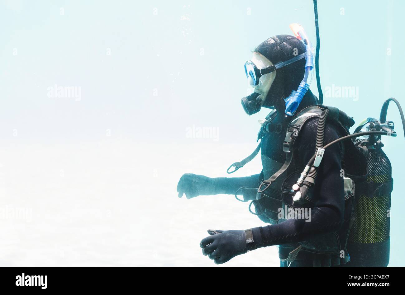 Plongeur portant un équipement de plongée complet avec masque, régulateur et BCD dérivant dans l'eau bleu-vert clair Banque D'Images