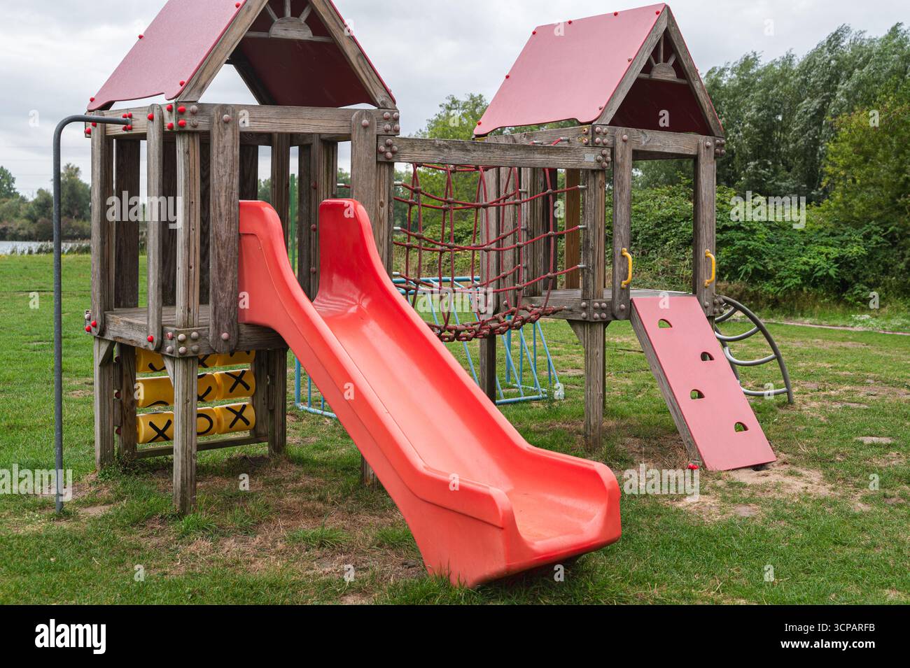 Cette aire de jeux animée dispose d'un grand toboggan rouge et de structures d'escalade dans une zone herbeuse pour les enfants et les familles Banque D'Images