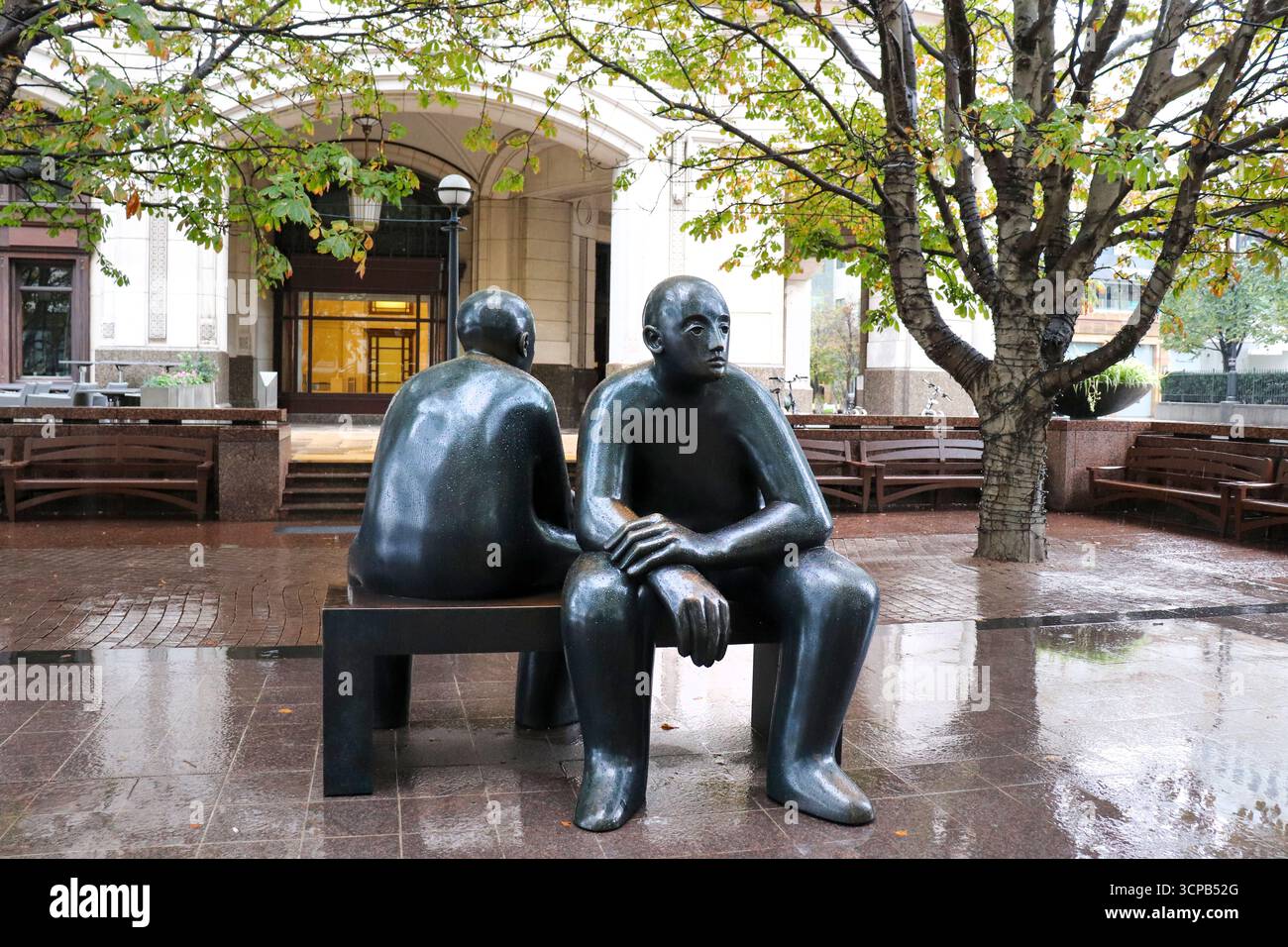Une statue de bronze intitulée Two Men on a Bench par l'artiste Giles Penny se trouve sur une place à Canary Wharf comme une exposition d'art en plein air Banque D'Images