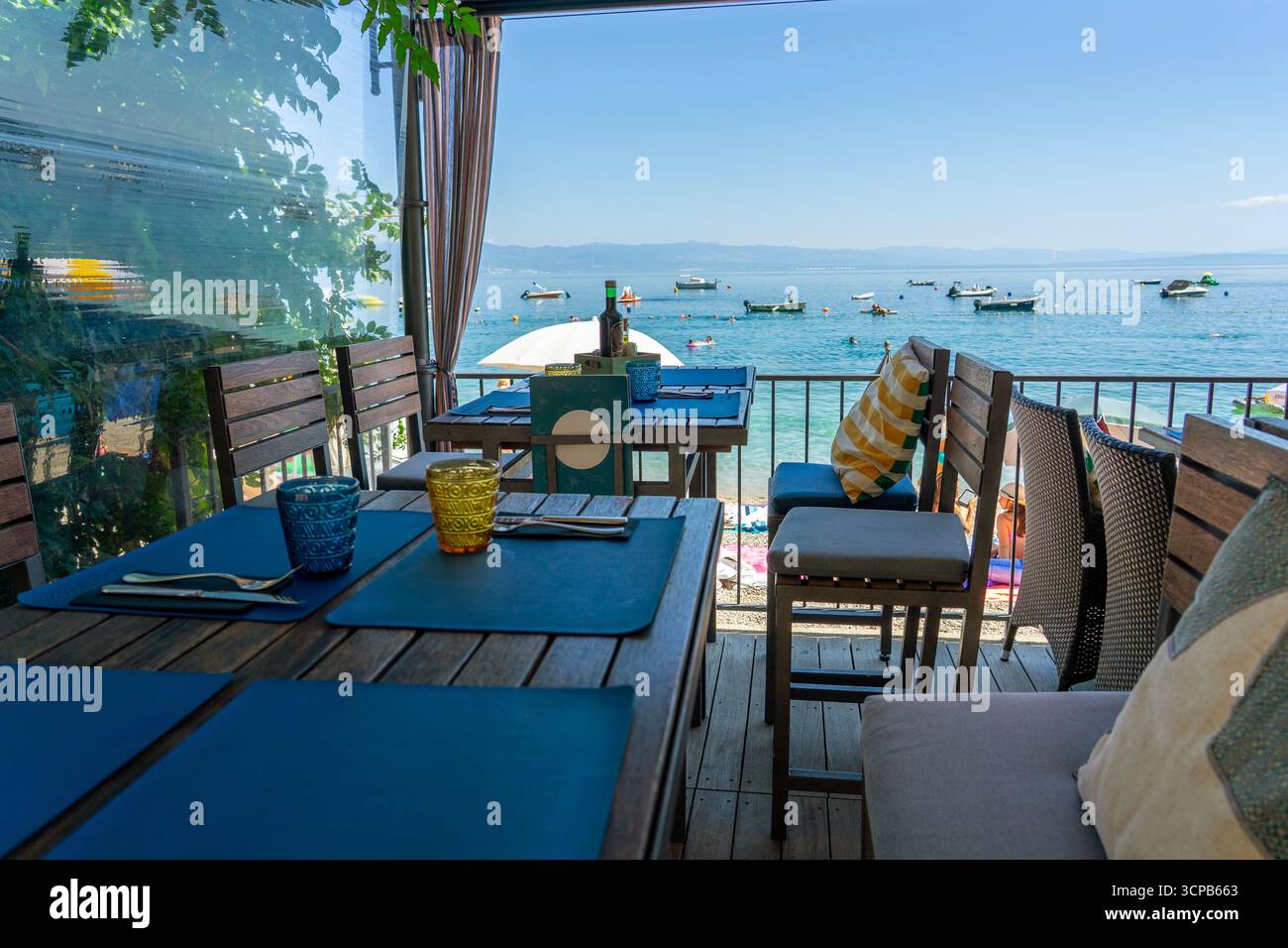 Terrasse de café en bord de mer avec tables et vue sur l'océan, parasols de plage et bateaux à proximité Banque D'Images