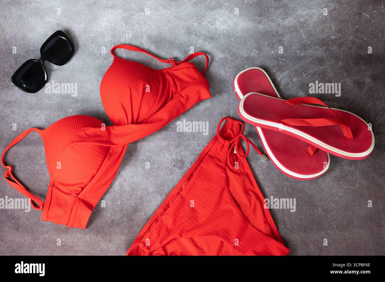 Portez un bikini rouge vif associé à des lunettes de soleil chics et des tongs confortables pour profiter pleinement des journées d'été Banque D'Images