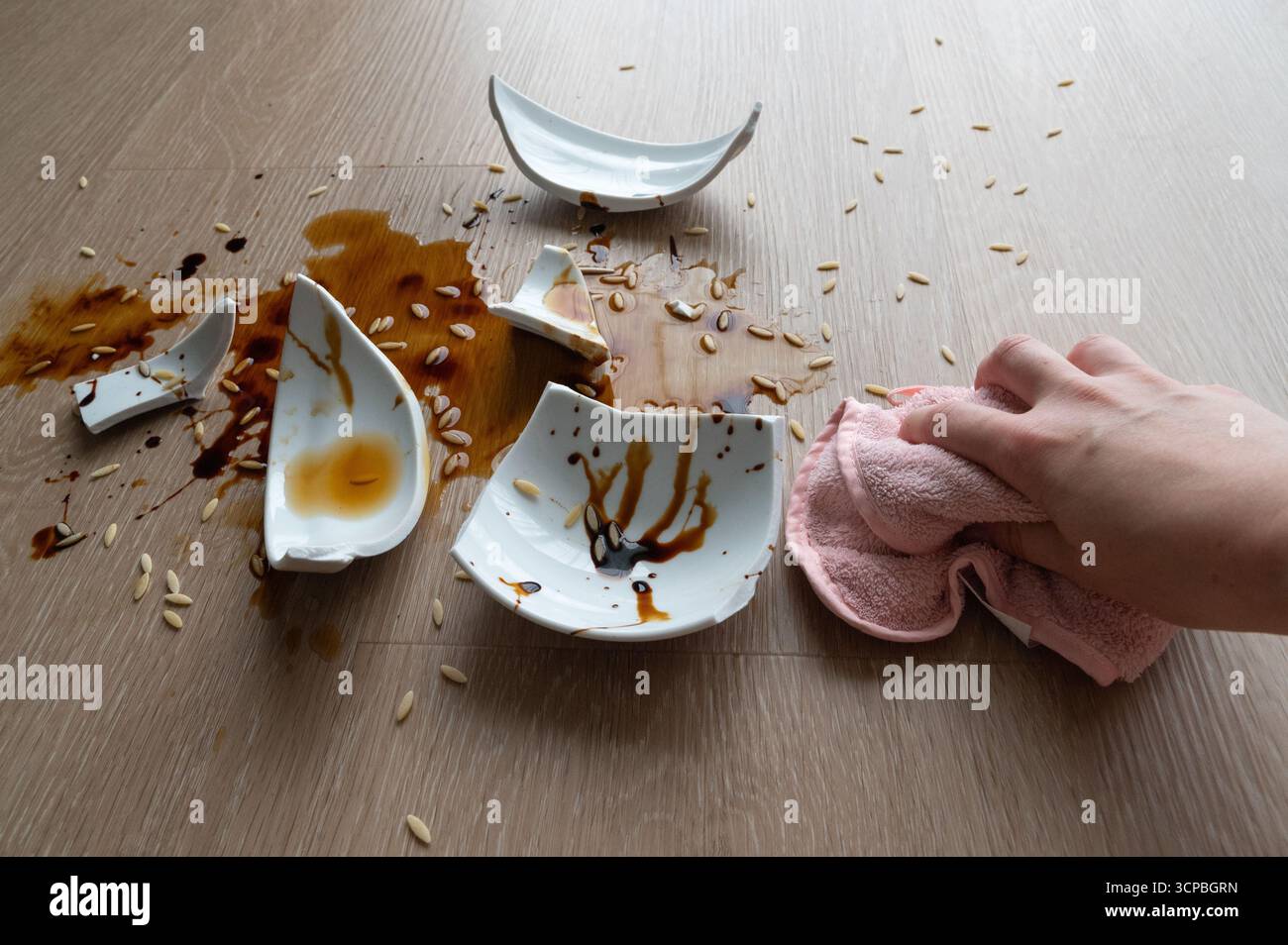 Une main essuie diligemment les éclats d'assiettes cassées et la sauce renversée d'une table après un malheureux accident Banque D'Images