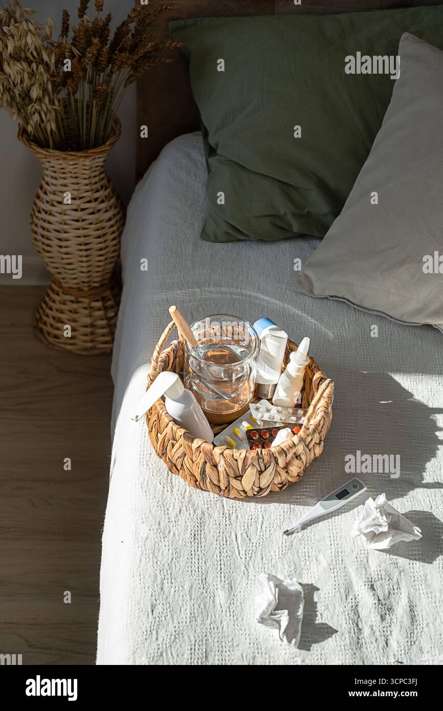 Panier en osier avec médicaments, pilules, eau et thermomètre sur le lit. Maladie, grippe et traitement du rhume. Concept de soins de santé et de récupération. Banque D'Images