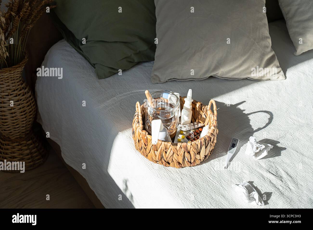 Panier en osier avec médicament, verre d'eau, thermomètre sur le lit. Concept de récupération quotidienne de la maladie. Traitement du rhume et de la grippe. Banque D'Images