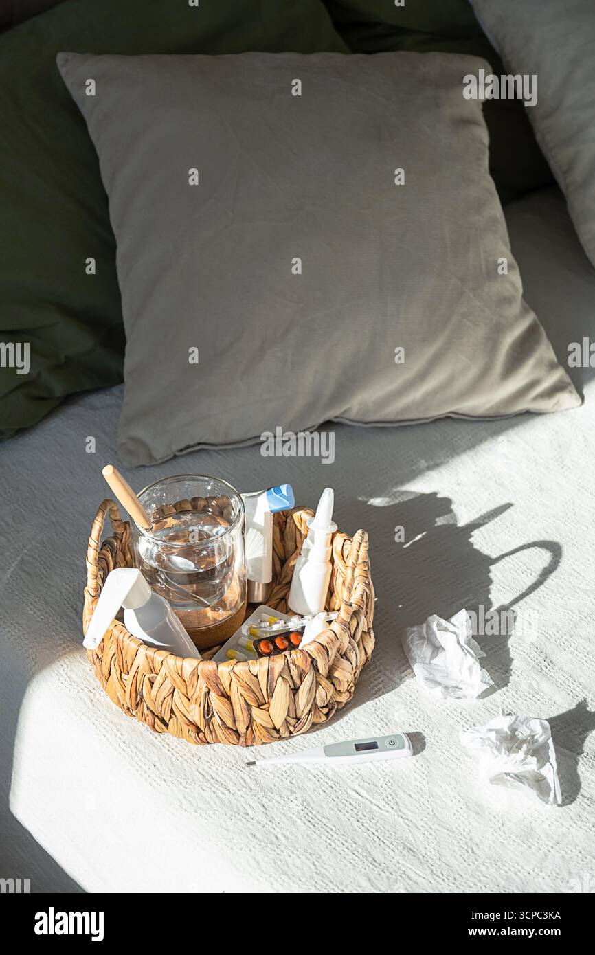 Panier en osier avec médicaments, verre d'eau et thermomètre sur couvre-lit blanc. Traitement du rhume et de la grippe. Maladie et concept de maladie. Banque D'Images