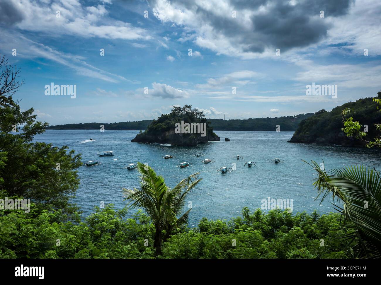 Paysage pittoresque plage de Pandan au nord-ouest de Nusa Penida, Bali, Indonésie. Petit îlot au milieu, bateaux amarrés dans la baie, forêt tropicale. Banque D'Images