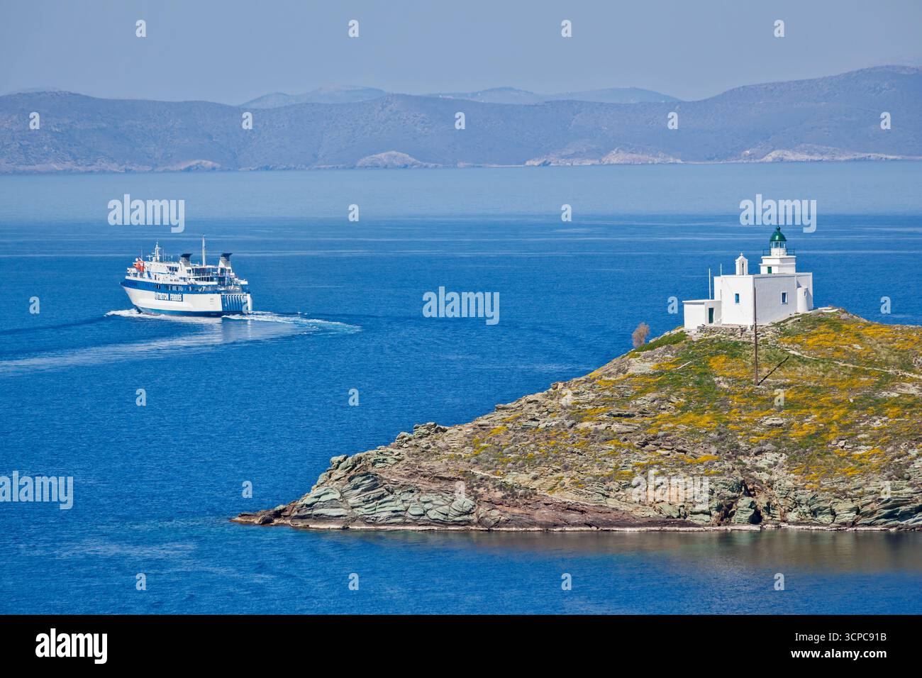Vue panoramique d'un ferry passant devant un phare blanc sur la côte rocheuse de l'île de Tzia en Grèce, avec la mer Égée bleu profond et la montagne lointaine Banque D'Images