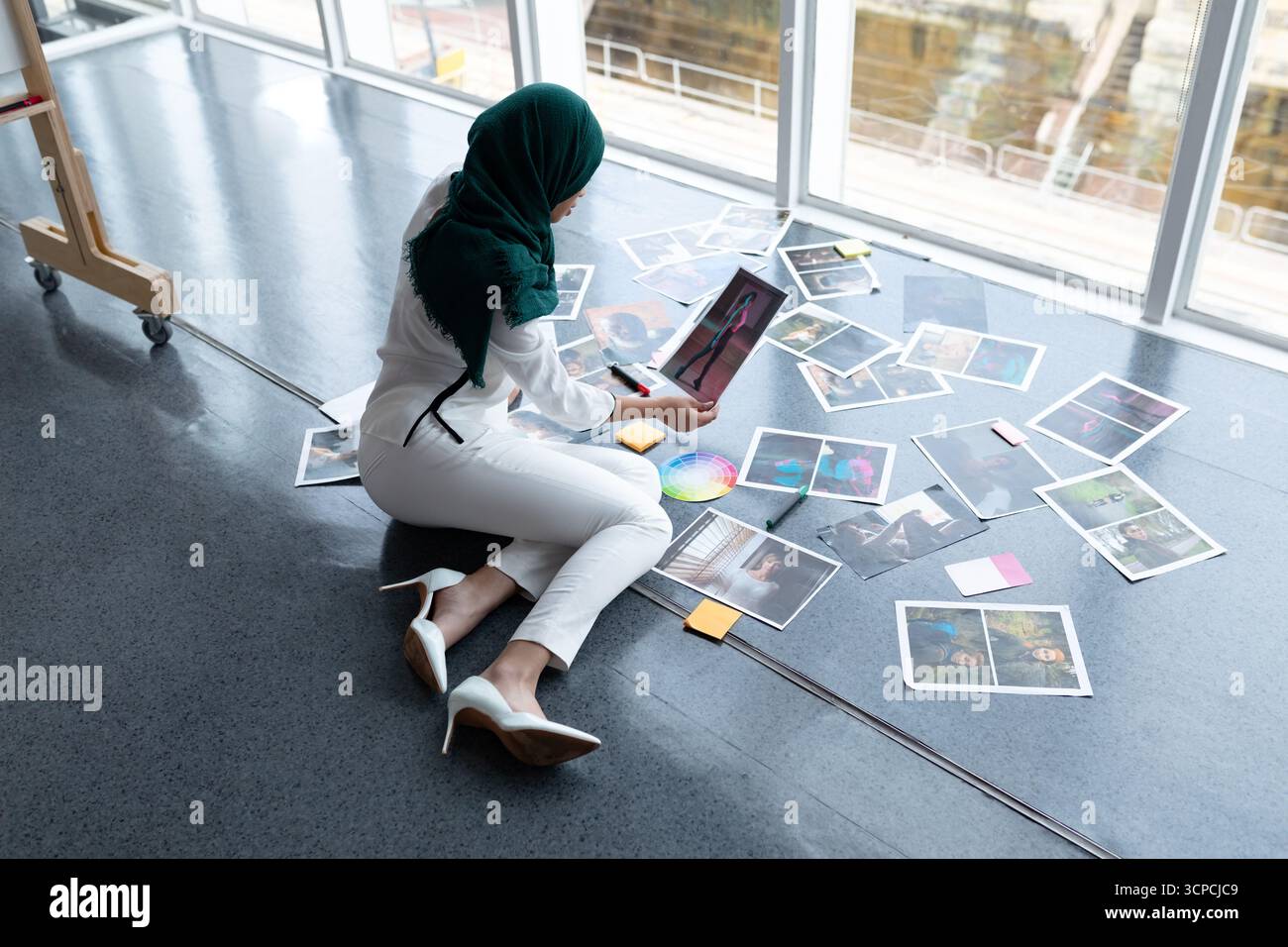 Femme hijabi du moyen-Orient assise sur le sol du studio, examinant les impressions, la roue des couleurs et les notes autocollantes Banque D'Images