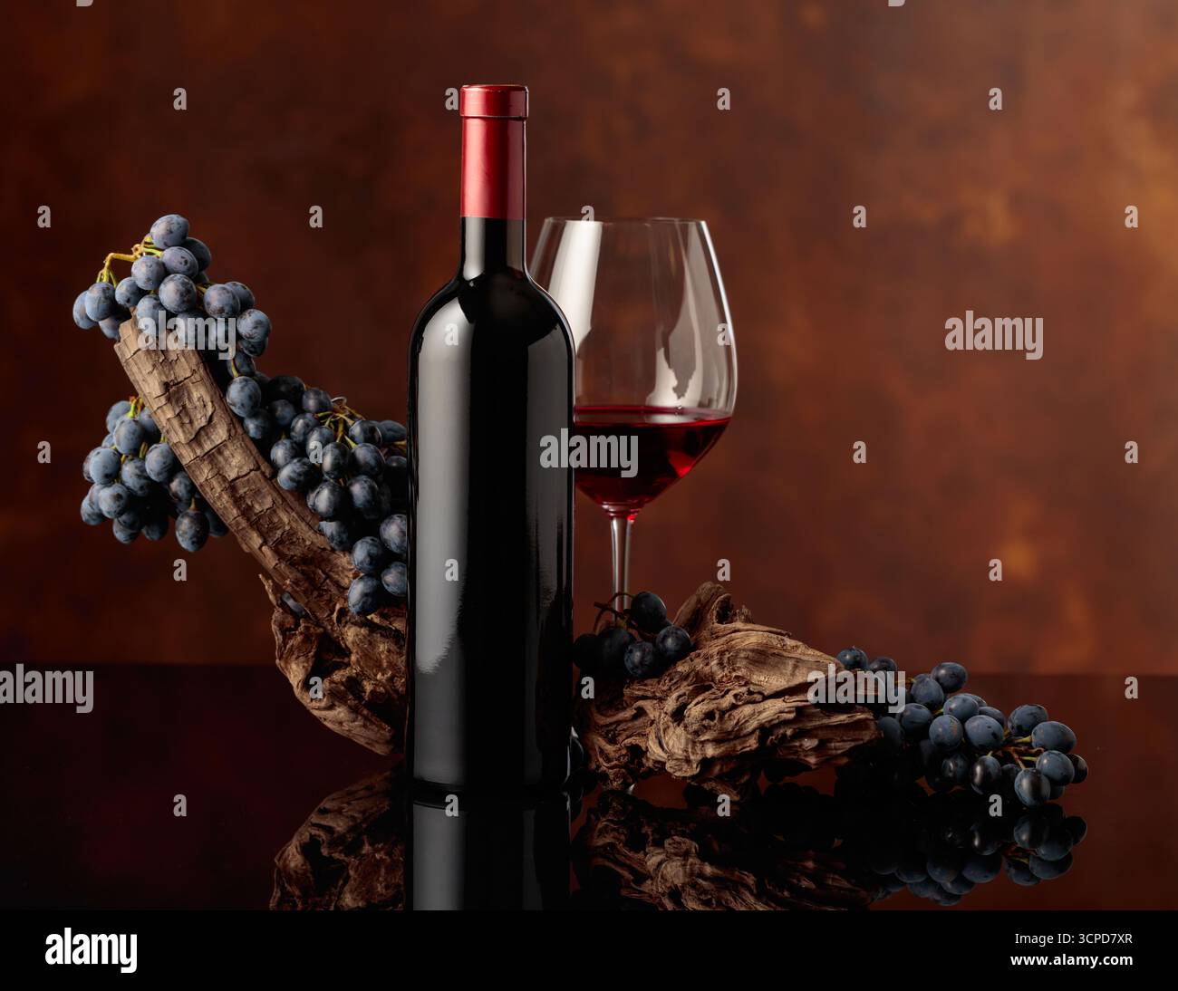 Vin rouge versé dans un verre à côté d'une bouteille sur un fond noir réfléchissant. Vin rouge avec un accroc altéré et raisins bleus sur un fond brun. Banque D'Images