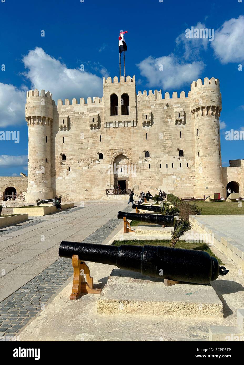 Alexandrie, Égypte - 13 février 2025 : visiteurs à la citadelle médiévale de Qaitbay forteresse avec drapeau égyptien et canons exposés. Banque D'Images